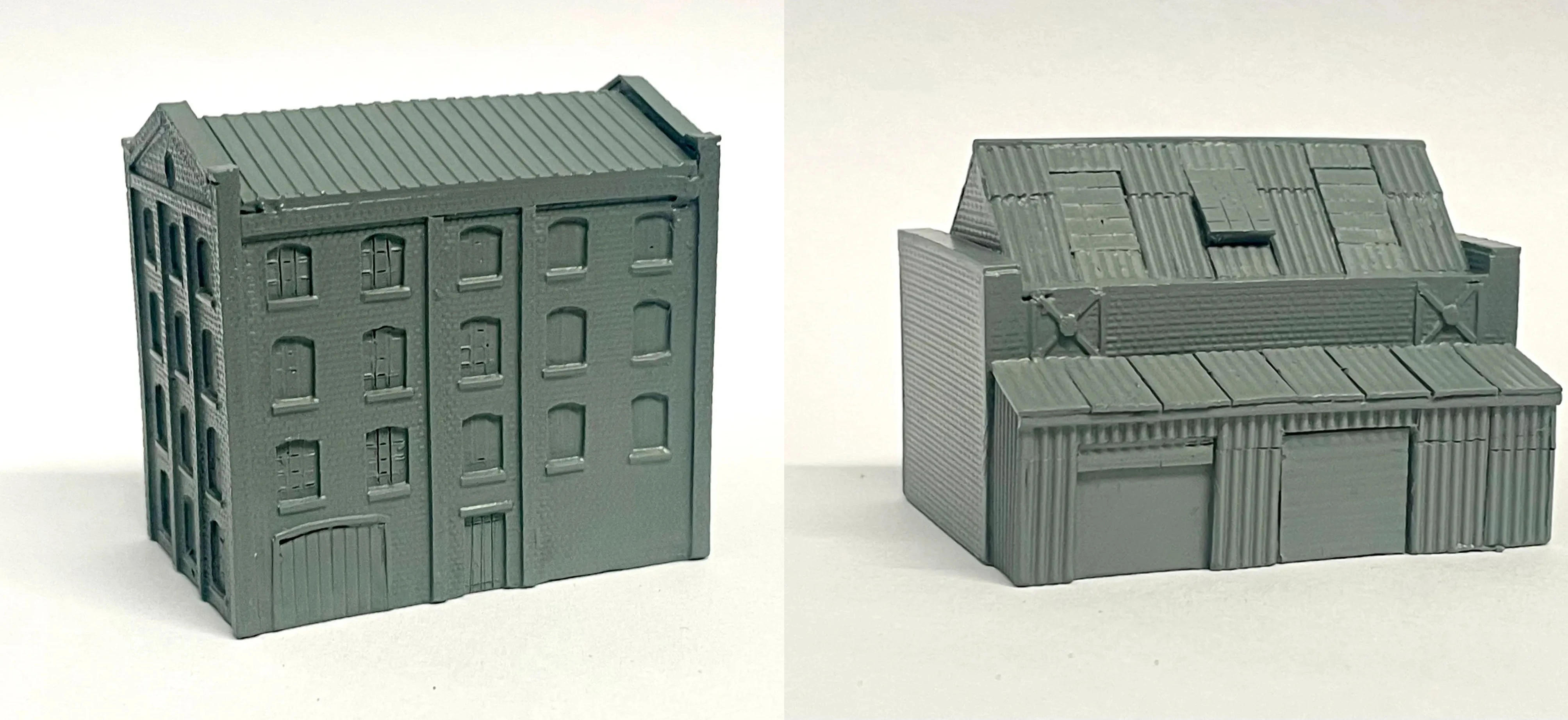 A detailed model of an industrial building designed for 6mm scale wargames, featuring a textured brick facade and multiple windows. The structure has a flat roof with visible paneling and a large door on the front, along with smaller doors and windows on the sides. The model is cast in a gray resin, showcasing its intricate design suitable for historical or modern warfare settings.