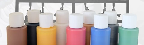 A collection of nine bottles of water-based acrylic paints in various colors, including black, white, dark green, mid blue, bright red, golden yellow, leather brown, bright gold, and chain mail, is displayed in the foreground. Behind the paint bottles is a sprue containing two Viridian Interdicts Marines, showcasing various miniature parts. A high-quality synthetic brush is positioned in front of the paint bottles, emphasizing the set's painting essentials.