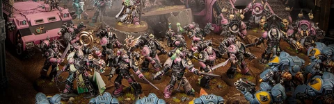 The image features a dynamic scene filled with a multitude of Emperor’s Children miniatures from the Warhammer 40,000 universe, showcasing their vibrant pink and purple color scheme. In the foreground, a diverse array of Chaos Space Marines, adorned with ornate armor and chaotic symbols, engage in battle, while a towering, menacing figure looms behind them, possibly a Daemon Engine or a warlord. Several vehicles, including armored transports, are also present, adding to the chaotic atmosphere of the battlefield, which is set against a dark, atmospheric backdrop. The overall composition emphasizes the flamboyant and hedonistic nature of the Emperor’s Children, reflecting their devotion to Slaanesh.