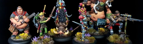 A group of eight intricately painted Moonstone miniatures stands against a black background. The characters include a muscular figure with a weapon, a green-skinned goblin in colorful attire, a knight in armor, and various other fantastical beings, each displaying unique features and vibrant colors. They are positioned on circular bases adorned with tufts of grass and small flowers, showcasing the detailed artistry of the miniatures.