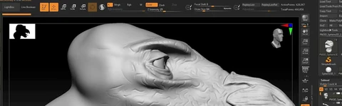 A close-up view of a digital sculpting project in ZBrush, showcasing a stylized dinosaur head. The model is primarily in a gray, untextured state, highlighting the intricate details of the scales and facial features, including a prominent eye and sharp teeth. The interface of ZBrush is visible at the top, displaying various sculpting tools and settings.