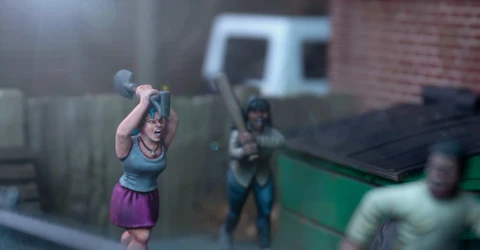 A dynamic scene features three miniature figures in a tense urban setting. In the foreground, a woman with blue hair raises a shovel, while a second figure behind her holds a baseball bat, both appearing ready to confront a threat. A third figure, dressed in a light shirt and blue pants, is seen running away, adding to the sense of urgency in the scene, with a green dumpster and a wooden fence in the background.