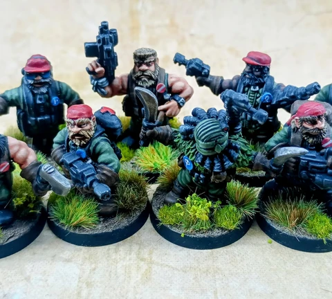 A group of eight intricately detailed miniatures representing space dwarves in a jungle setting, each standing on circular bases adorned with tufts of grass. The figures are dressed in military-style attire, featuring green clothing and red caps, with various weapons including guns and a curved blade. Their expressions are fierce and determined, showcasing a blend of ruggedness and character typical of old-school metal miniatures.