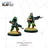 Two miniature commandos are depicted in an advancing pose, ready for action. The first commando, on the left, has dark skin and wears a green hat, a green and black uniform, and holds a futuristic weapon. The second commando, on the right, has light skin, wears a gray cap and a green uniform, and also carries a similar weapon. Both figures stand on bases with tufts of grass, set against a grid-like background.