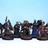 A diverse group of painted miniatures stands against a light blue background, showcasing various adventurers and characters. The figures include a mix of warriors, spellcasters, and rogues, each detailed with unique clothing, weapons, and expressions. They are mounted on circular bases with tufts of grass, highlighting their fantasy theme and adding to the overall aesthetic of the collection.