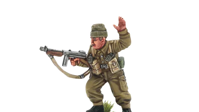 A detailed miniature of a soldier in a military uniform, standing on a circular base adorned with grass and dirt. The figure, representing Augustus Newman VC, is depicted in a dynamic pose, holding a submachine gun in one hand while raising the other in a commanding gesture. He wears a green beret and a khaki uniform, complete with various pouches and gear attached to his chest.