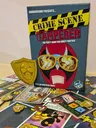 Crime Scene Tamperer game box with cards and tokens scattered on a wooden floor.