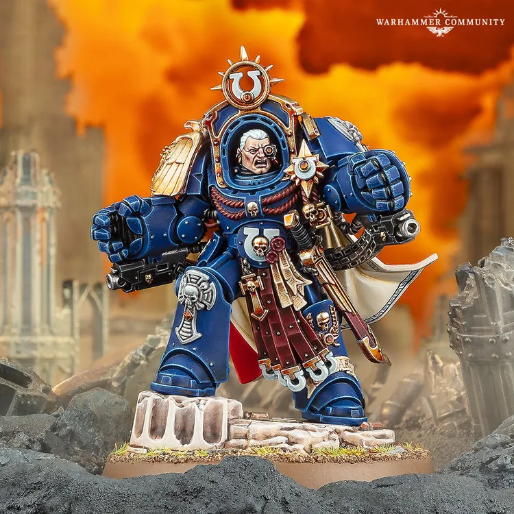A detailed miniature of Marneus Calgar stands prominently, clad in blue power armor adorned with gold and red embellishments. He holds a bolter in one hand and wears a distinctive helmet with a prominent emblem, while a flowing white cape adds to his imposing presence. The background features a dramatic, fiery explosion, enhancing the sense of battle and chaos surrounding him.