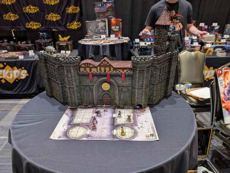 Model of Castle Ravenloft with miniatures on a map, WizKids banners in background.