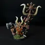 A miniature figure of a Chaos Dwarf with a long orange beard, wearing armor and holding a large axe in one hand and a staff topped with a ram's skull and circular blade in the other. The figure stands on a small base with green tufts of grass. The background is black.