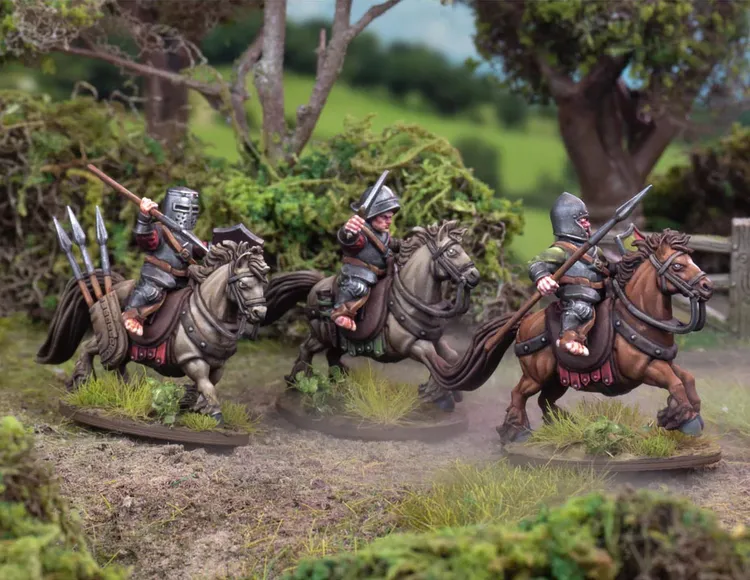 Three halfling cavalry figures are riding horses through a lush, green landscape. Each rider is equipped with different weapons: one holds a spear, another has a javelin, and the third carries a lance. The horses are adorned with saddles and gear, and the background features dense foliage and trees, enhancing the natural setting.