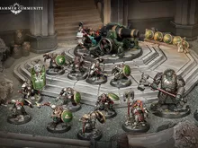 Miniature figures of armored duardin warriors in green and silver plate, standing on a rocky battlefield. One figure holds a large green banner with a white circular emblem. A cannon with a crew of two figures is positioned on a raised platform.