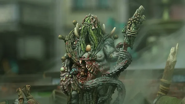 Green-skinned monster with long hair, horns, and a staff, holding a severed head.