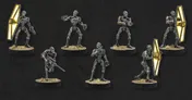 A collection of eight BX-Series Droid Commandos is displayed against a dark background, each standing on a circular base with tufts of grass. The droids are depicted in various poses, showcasing their sleek, metallic bodies with orange accents and distinct features, including weapons like blasters and a shield. This set highlights their versatility as both combatants and enforcers in the Star Wars: Legion game.