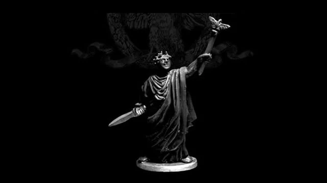 A 28mm scale miniature of Caesar Imperator stands prominently against a dark background. The figure is cast in white metal, showcasing intricate details such as a laurel crown and flowing robes. In one hand, he holds a sword, while the other is raised, delicately supporting a butterfly, symbolizing peace or transformation. The base is circular, providing stability to the figure, which is sculpted with a sense of grandeur and historical significance.