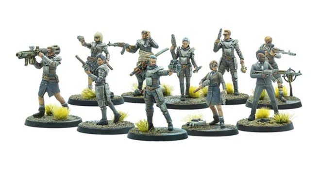 The image features a group of ten intricately detailed, 32mm-scale miniatures from the Fallout: Factions starter set. Each figure is posed dynamically, showcasing a variety of weapons and attire that reflect a post-apocalyptic aesthetic, with muted colors and weathered textures. The miniatures stand on circular bases adorned with tufts of green grass, enhancing the scene's rugged, irradiated environment.