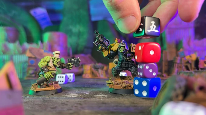 Two colorful orc miniatures stand in a chaotic urban setting, one holding a gun and the other brandishing a weapon, both poised for action. A hand is seen stacking various dice, including black, red, and blue, creating a precarious tower beside them. The background features a vibrant, cluttered environment with hints of a megacity, enhancing the playful and chaotic atmosphere of the game.