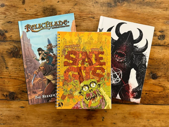 Three tabletop gaming books are displayed on a wooden surface. The book on the left is titled "Relicblade: The Seeker's Guide," featuring a colorful cover with a fantasy theme. The central book, "SPACE GITS," has a vibrant, cartoonish cover depicting a green orc with glasses, surrounded by chaotic illustrations. On the right, a darker book features a menacing figure with horns and a pentagram, suggesting a more sinister theme.