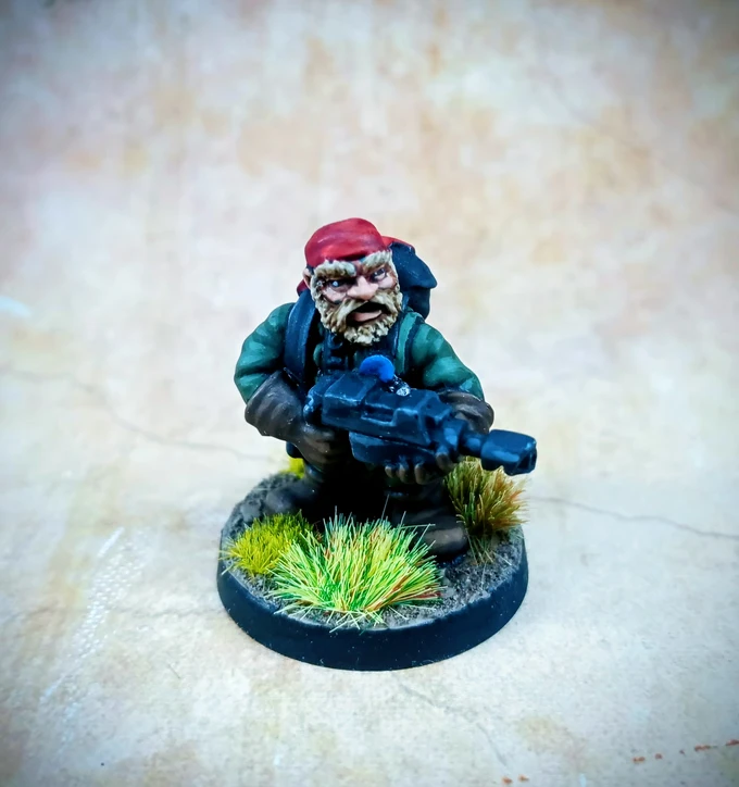 A detailed miniature of a rugged space dwarf stands in a dynamic pose, holding a futuristic weapon. He wears a red bandana, a green jacket, and has a scruffy beard, conveying a tough, battle-ready appearance. The base features tufts of green grass, enhancing the jungle theme, against a softly blurred background.