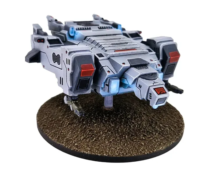 A detailed model of a sci-fi vehicle, resembling a futuristic dropship, is displayed on a circular base with a textured, brown surface. The vehicle features a sleek, angular design with a predominantly gray color scheme, accented by red and blue highlights. It has multiple thrusters and mechanical appendages, suggesting advanced technology suitable for interstellar combat.