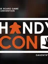 White text on dark background reads "UK BOARD GAME CONVENTION." Large orange and white text spells "HANDYCON" with an orange icon of a person in a wheelchair between letters. To the right, an orange hand icon. Small white text at bottom reads "DAVENTRY, UK."