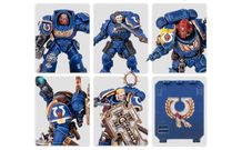 A collection of Ultramarine miniatures showcases various Space Marine figures in blue armor, each featuring distinct details and accessories. The top row includes a character with a prominent helmet and ornate chest emblem, alongside two other figures with different poses and weaponry. The bottom row features a close-up of a figure holding a weapon, another with a skull motif on the armor, and a character wielding a large, intricately designed shield. Additionally, a transfer sheet with various decals is visible, featuring Ultramarine symbols and decorative borders.