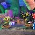 Two colorful orc miniatures stand in a chaotic urban setting, one holding a gun and the other brandishing a weapon, both poised for action. A hand is seen stacking various dice, including black, red, and blue, creating a precarious tower beside them. The background features a vibrant, cluttered environment with hints of a megacity, enhancing the playful and chaotic atmosphere of the game.