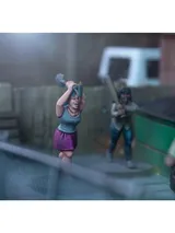 A dynamic scene features three miniature figures in a tense urban setting. In the foreground, a woman with blue hair raises a shovel, while a second figure behind her holds a baseball bat, both appearing ready to confront a threat. A third figure, dressed in a light shirt and blue pants, is seen running away, adding to the sense of urgency in the scene, with a green dumpster and a wooden fence in the background.