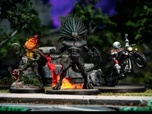 Two miniature figures on bases: one with a skeletal, armored design, glowing red flames on head and chest, holding a hammer, standing on a rocky surface; another with a muscular, black-skinned figure with a spiked helmet, flexing arms, surrounded by fire.