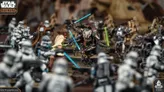 A dynamic scene from Star Wars Legion features a clash between Clone Troopers and droids, with General Grievous prominently wielding blue lightsabers. In the foreground, several Clone Troopers are poised for battle, while Obi-Wan Kenobi, dressed in a beige robe, engages with Grievous. The background is filled with additional droids and soldiers, creating a sense of action and conflict.