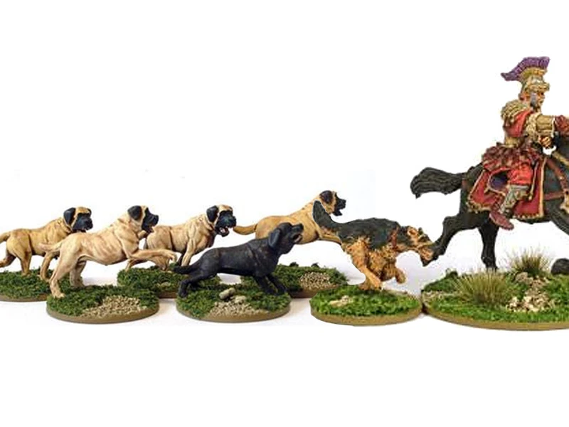 A collection of miniature dogs in various poses, including several tan and black dogs, is displayed on grassy bases. In the background, a mounted Roman general in ornate armor and a colorful plume rides a horse, adding a historical element to the scene. The dogs appear to be interacting with each other, creating a lively atmosphere around the general.