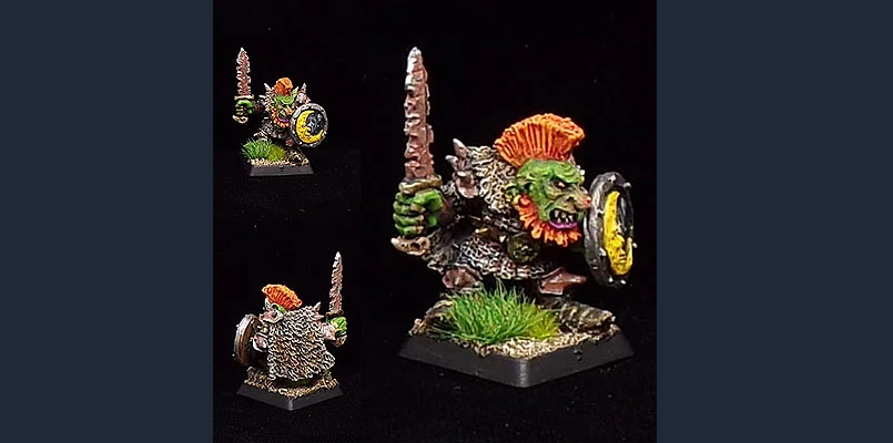 The image features a dynamic goblin miniature, showcasing vibrant colors and intricate details. The goblin, with green skin and a bright orange mohawk, wields a sword in one hand and a shield in the other, displaying a fierce expression. It stands on a textured base adorned with tufts of grass, emphasizing its battle-ready stance. The miniature is presented from multiple angles, highlighting its character and craftsmanship.
