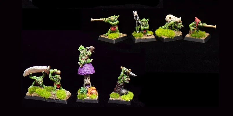 A collection of dynamic goblin miniatures is displayed, showcasing their vibrant green skin and various poses. The goblins are set on textured bases with tufts of grass, enhancing their whimsical character. Notable figures include a goblin playing a musical instrument, one wielding a large weapon, and another standing atop a mushroom, all contributing to the playful and mischievous theme typical of Kev Adams' designs.
