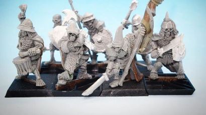 A collection of 28mm scale skeleton warriors from Diehard Miniatures, featuring several figures in various poses. The miniatures are equipped with weapons such as spears and swords, and are adorned with armor and helmets reminiscent of classic Oldhammer designs. The background is a soft blue gradient, highlighting the details of the skeletal figures, which are mounted on black bases.