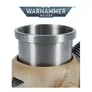 Silver metal mug with a smooth, reflective surface, featuring a rolled rim and a black coiled cord attached to its side. The mug sits atop a beige, textured object resembling a stylized skull, which has a small rectangular plate with three bolts on its side. In the background at the top, a metallic banner displays the text "WARHAMMER 40,000" in bold, futuristic lettering.