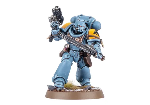 A Space Wolf Blood Claw miniature stands in a dynamic pose, wielding a chainsword in one hand and a pistol in the other. The miniature is painted in a striking blue color with yellow shoulder pads, showcasing intricate details and textures. It is mounted on a round base with a grassy terrain effect, emphasizing its role in the Warhammer 40,000 universe.