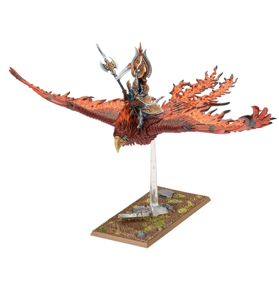 A majestic Flamespyre Phoenix, with vibrant red and orange plumage, soars through the air, carrying a mounted high-elf lord adorned in intricate armor. The phoenix's wings are outstretched, showcasing detailed feather patterns, while the rider holds a spear, ready for battle. The model is mounted on a clear stand, positioned above a base featuring rocky terrain and patches of grass.