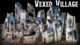 A collection of quirky, ramshackle buildings from the Vexed Village set, featuring skewed proportions and angles that create a surreal aesthetic. The structures are predominantly white with blue roofs, showcasing a mix of intact and ruined designs, including crumbling walls and a partially destroyed tower. The title "Vexed Village" is prominently displayed at the top in bold, stylized lettering against a dark background.