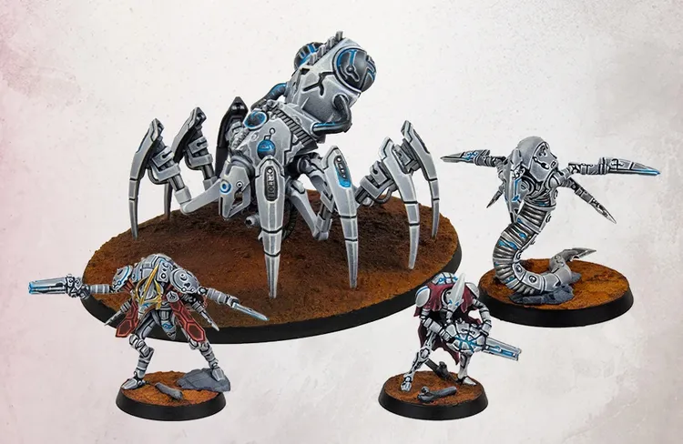 A collection of intricately designed miniatures from the Robot Legions faction, featuring a large, spider-like robot with multiple legs and a sleek, metallic finish, alongside smaller robotic figures in dynamic poses. The miniatures are set against a textured, brown base that resembles a barren landscape. The color palette includes shades of silver and blue, highlighting the futuristic and sci-fi aesthetic of the models.