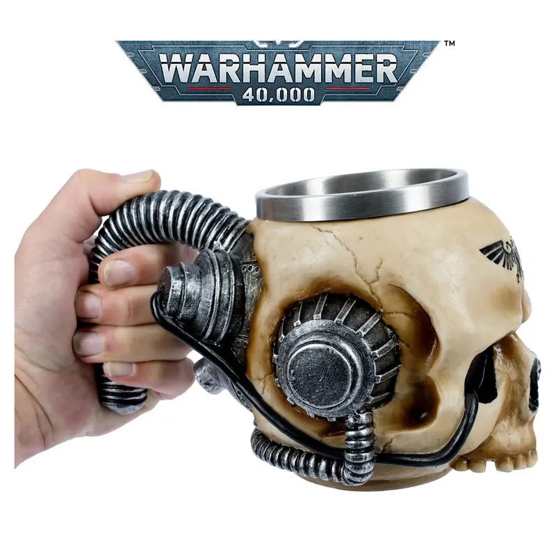 A hand holds a detailed model of a servo skull from the *Warhammer 40,000* universe. The skull is beige with mechanical components attached, including a metallic cylindrical cup embedded in the top of its cranium. A flexible, coiled cable extends from the back of the skull, wrapped around the hand’s fingers. On the side of the skull, near the temple, is a small black Imperial Aquila symbol. Above the image, a metallic banner displays the text: "WARHAMMER 40,000" in bold, silver letters.