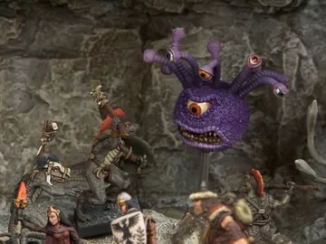 A collection of fantasy miniatures features several lizardmen, one wielding a shield and weapon, and another with a torch, set against a rocky backdrop. In the background, a large, purple creature with multiple eyes and a menacing expression looms, adding to the scene's fantastical atmosphere. A female character in dark robes stands nearby, while other figures in armor are partially visible, enhancing the sense of adventure.
