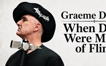 Man in black beret with bat pins, wearing a metal device with coiled cord around neck.