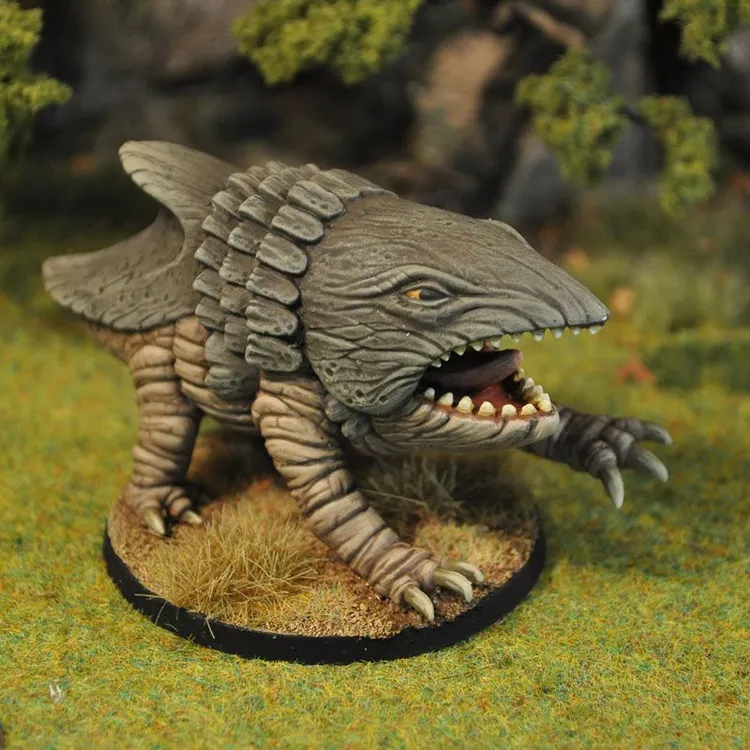 A detailed miniature of a creature resembling a prehistoric reptile, featuring a textured gray body with prominent scales and a large, toothy mouth. It stands on a circular base covered with a sandy texture and tufts of grass, set against a blurred natural backdrop of greenery. The creature has a distinctive head with a shark-like shape and small, fierce eyes, showcasing intricate sculpting and paintwork.