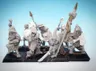 A collection of 28mm scale skeleton warriors from Diehard Miniatures, featuring several figures in various poses. The miniatures are equipped with weapons such as spears and swords, and are adorned with armor and helmets reminiscent of classic Oldhammer designs. The background is a soft blue gradient, highlighting the details of the skeletal figures, which are mounted on black bases.