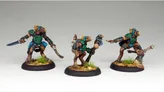 Three intricately painted miniatures stand on a textured base with tufts of grass. Each figure features a humanoid creature with a brown body, adorned with vibrant blue and green armor and accessories. The leftmost figure wields a curved sword, the center figure holds a staff with a small creature perched on top, and the rightmost figure points forward, showcasing their unique designs and expressions.