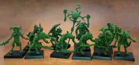 A collection of old school miniatures from Satyr Art Studio, featuring various fantastical creatures in a vibrant green color. The figures include beastmen with distinct features such as horns and claws, some wielding weapons, and a central figure holding a staff topped with a skull and a crescent. They are displayed on black bases against a warm, textured background.