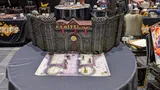 Model of Castle Ravenloft with miniatures on a map, WizKids banners in background.
