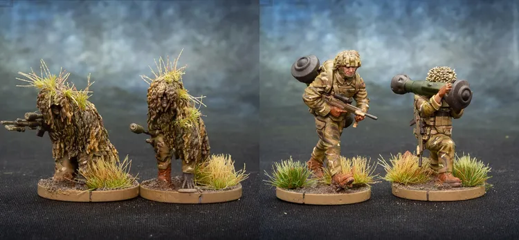 Two detailed miniature soldiers are depicted on circular bases with tufts of grass. The first soldier, on the left, is dressed in camouflage and carries a rifle, while a backpack is slung over his shoulder. The second soldier, on the right, is also in camouflage and is shouldering a weapon system, possibly a missile launcher, with foliage attached for camouflage. The background features a gradient of blue and gray, enhancing the focus on the miniatures.