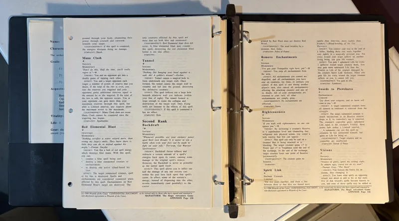 A three-ring binder containing pages from the playtest manuscript of "ManaStorm: The Magic Adventure Game." The visible pages feature spell descriptions, including "Mana Clash," "Red Elemental Blast," "Tunnel," and "Second Rank Backdraft," each detailing the spell's theory, effects, and counter effects. The text is printed in a clear font, with headings and sections organized for easy reference, and the pages are slightly worn, indicating their use in playtesting.