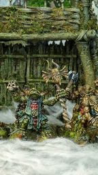 A group of intricately detailed miniatures inspired by Celtic mythology is displayed in front of a rustic, weathered structure covered in moss and foliage. The miniatures, depicting various fantastical creatures, include a central figure holding a banner, flanked by others wielding weapons and adorned with unique features like tusks and intricate patterns. The scene is set amidst a misty, ethereal atmosphere, enhancing the mystical theme of the Famhairean campaign.
